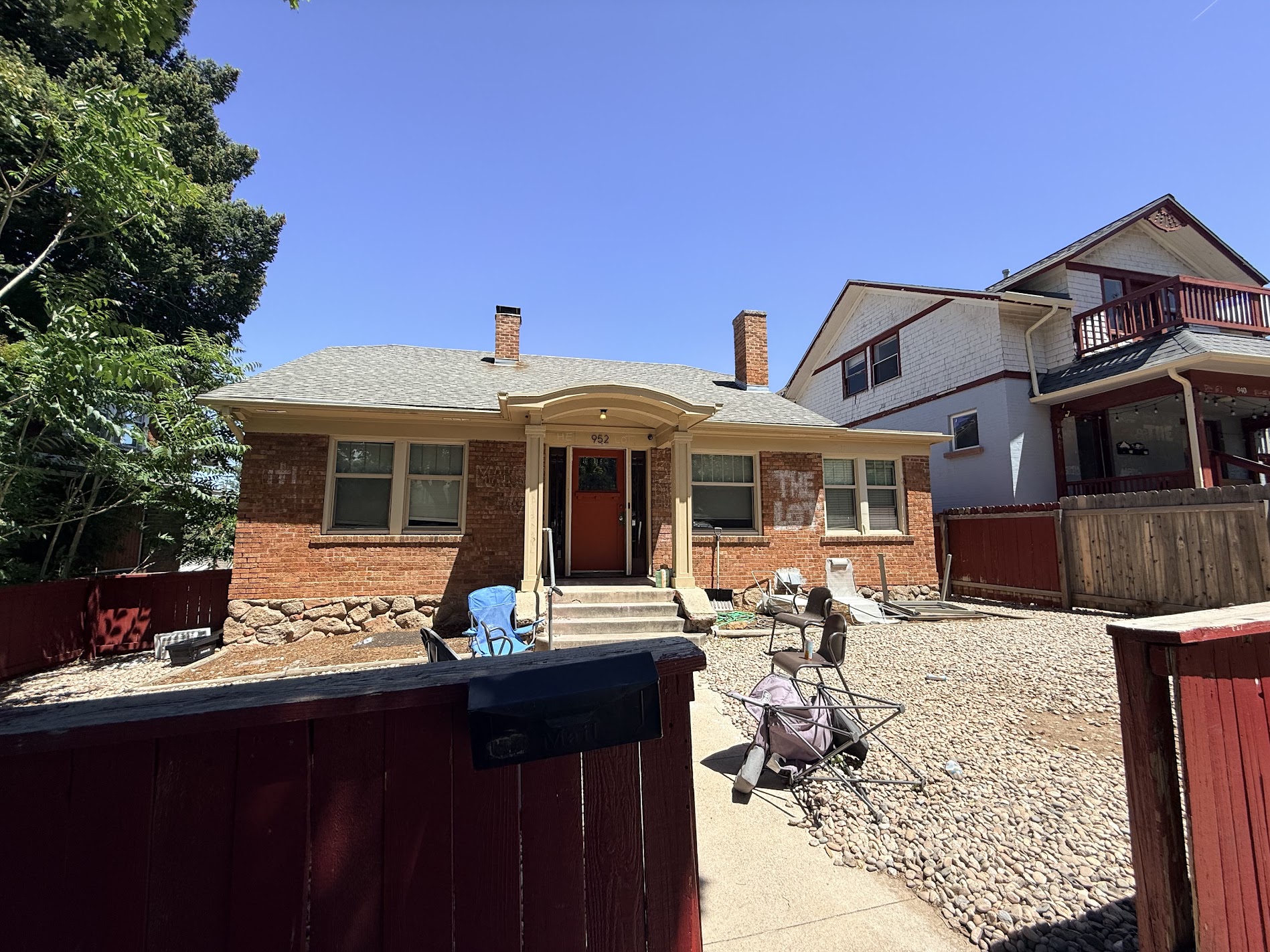 A brick bungalow with cream trim and a red front door during exterior painting