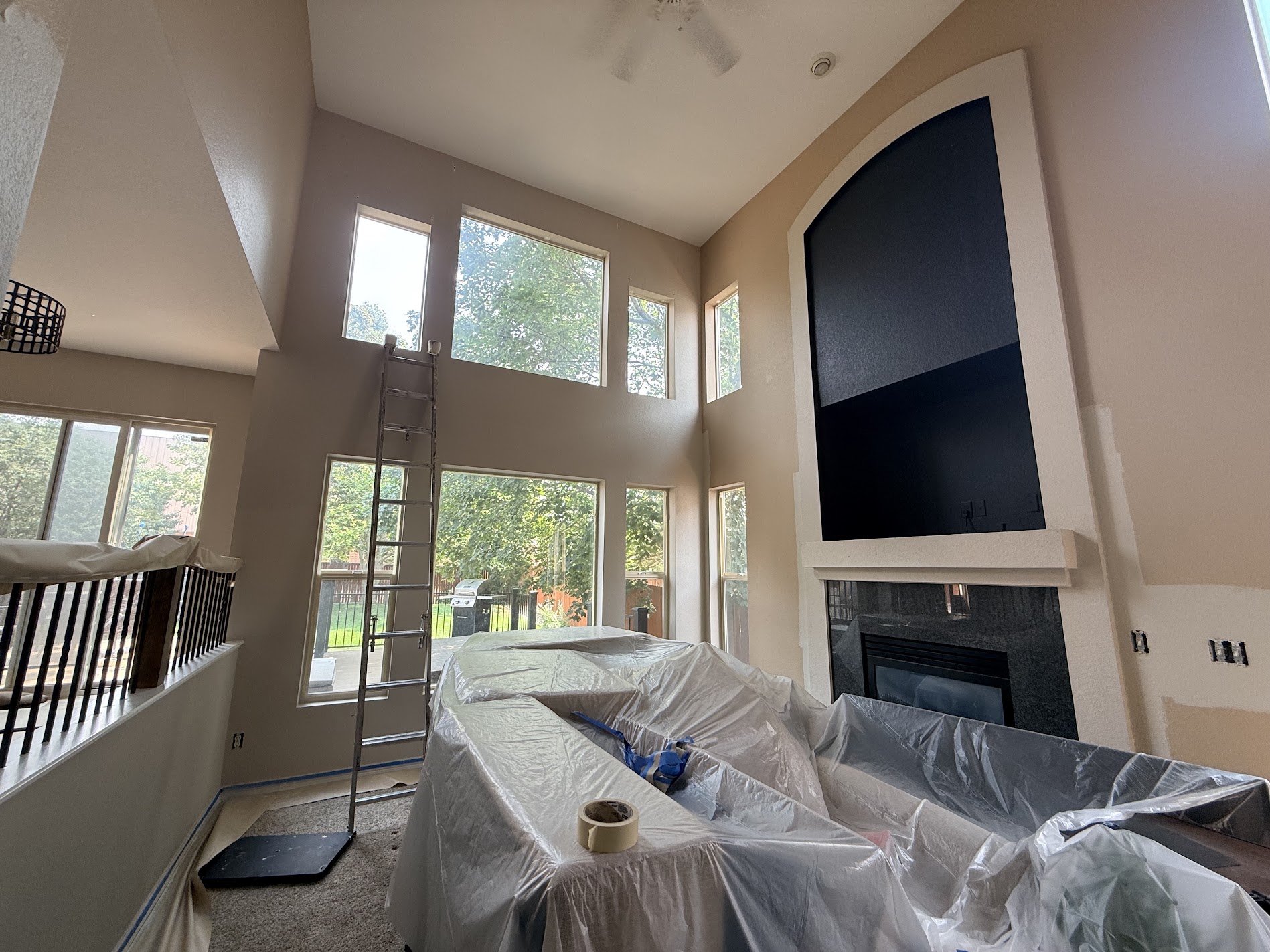 A vaulted living room mid-project with furniture covered and an extension ladder in place