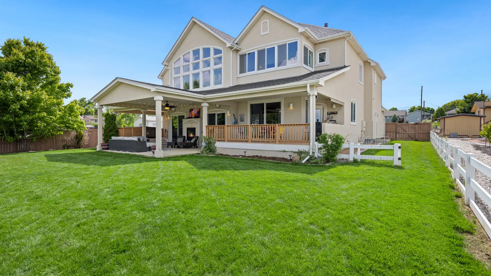 The back of a cream two-story house with a wrap-around porch and a white fence